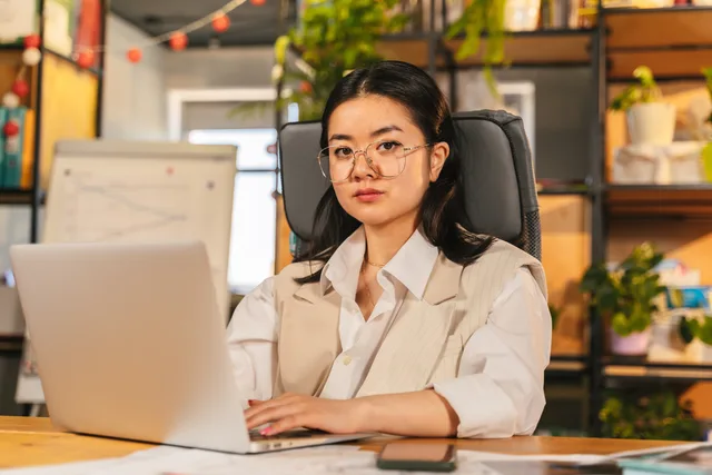 Confident businesswoman with glasses focusing on work using a laptop in a modern office setting. A procurement process for AI marketing tools
